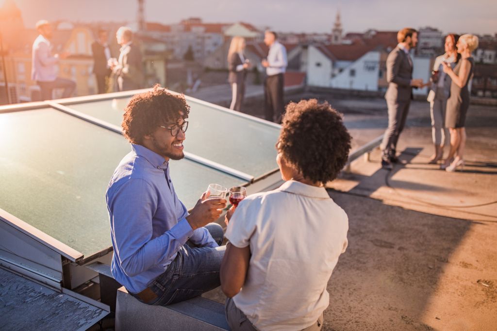 Happy African American man toasting with his female colleague during a party on a roof.