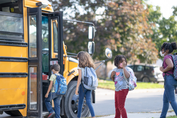 Multi ethnic elementary school students lining up to get into school bus during COVID-19