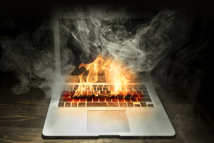 Close up laptop burned with flame and smokes on a wooden desk isolated over black background.