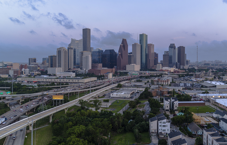 Katy Freeway traffic converge on metropolitan heart in Houston, Texas. Urban skyline towers over sprawling expanse.