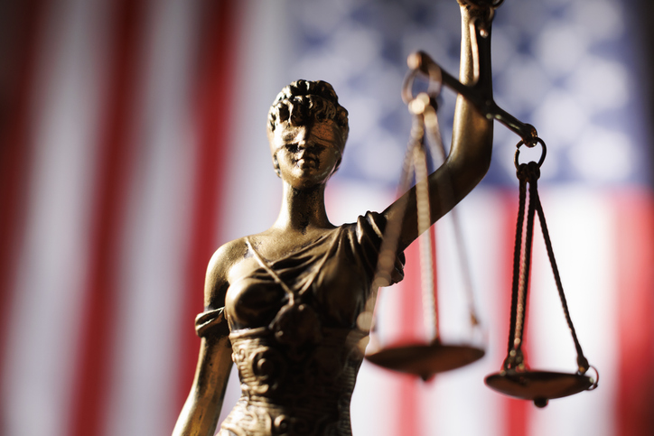Lady Justice figure holding scales in front of American flag representing law and order