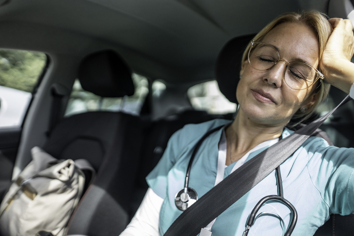 Tired female healthcare worker sleeping in parked car